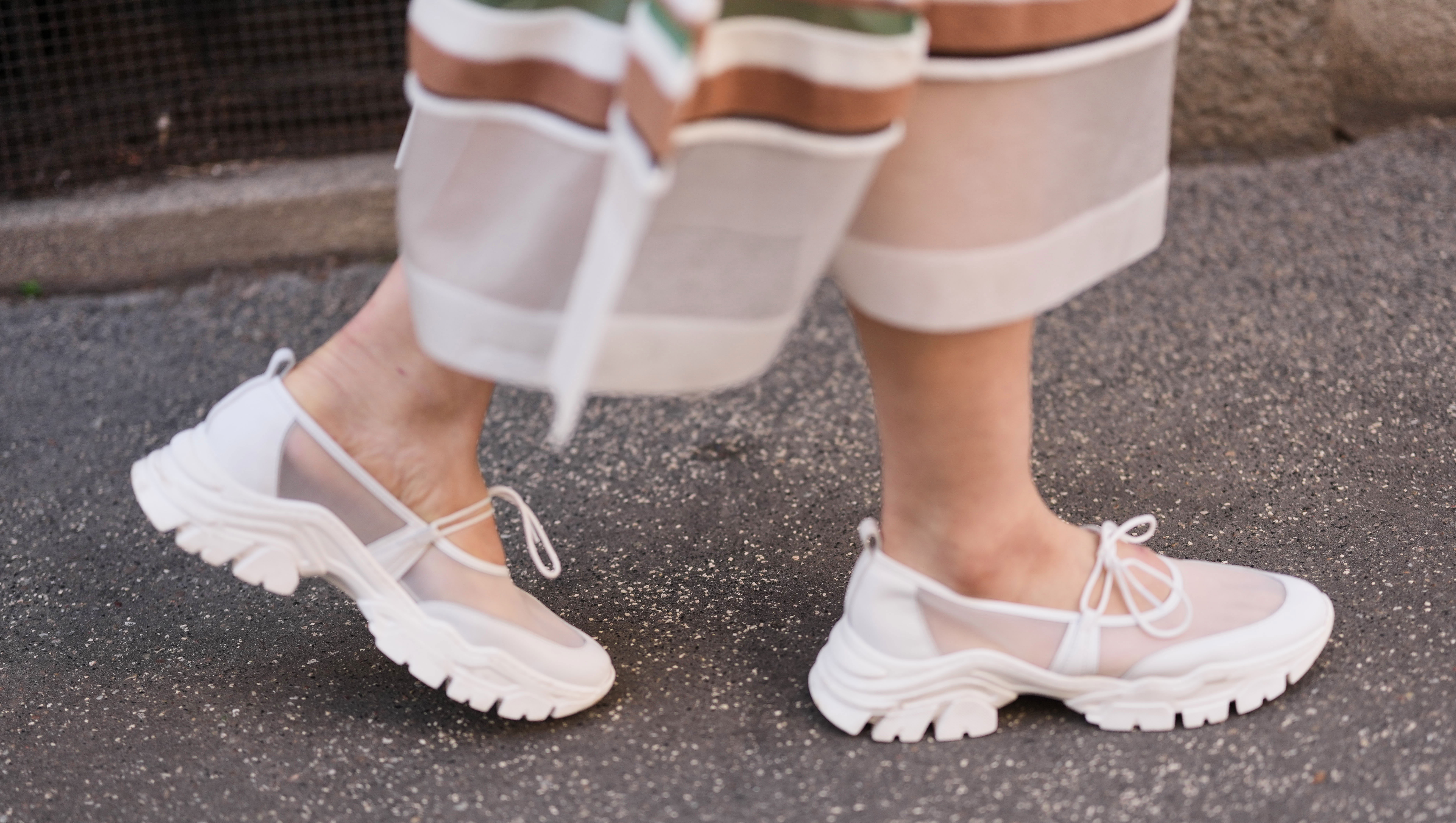 MILAN, ITALY - FEBRUARY 26: A guest wears white sheer mesh long skirt with opaque panels and multicolor striped trim at the hem in white / brown / and green, white mesh and leather chunky Mary Jane sneakers shoes with tie bows and thick tread soles, outside Anteprima, during Milan Fashion Week - Womenswear Fall/Winter 2026/2027, on February 26, 2026 in Milan, Italy (Photo by Edward Berthelot/Getty Images)