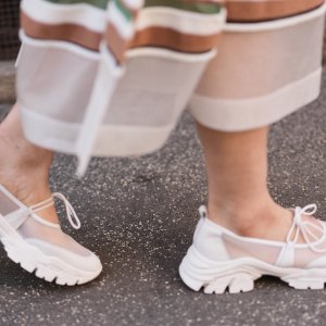 MILAN, ITALY - FEBRUARY 26: A guest wears white sheer mesh long skirt with opaque panels and multicolor striped trim at the hem in white / brown / and green, white mesh and leather chunky Mary Jane sneakers shoes with tie bows and thick tread soles, outside Anteprima, during Milan Fashion Week - Womenswear Fall/Winter 2026/2027, on February 26, 2026 in Milan, Italy (Photo by Edward Berthelot/Getty Images)