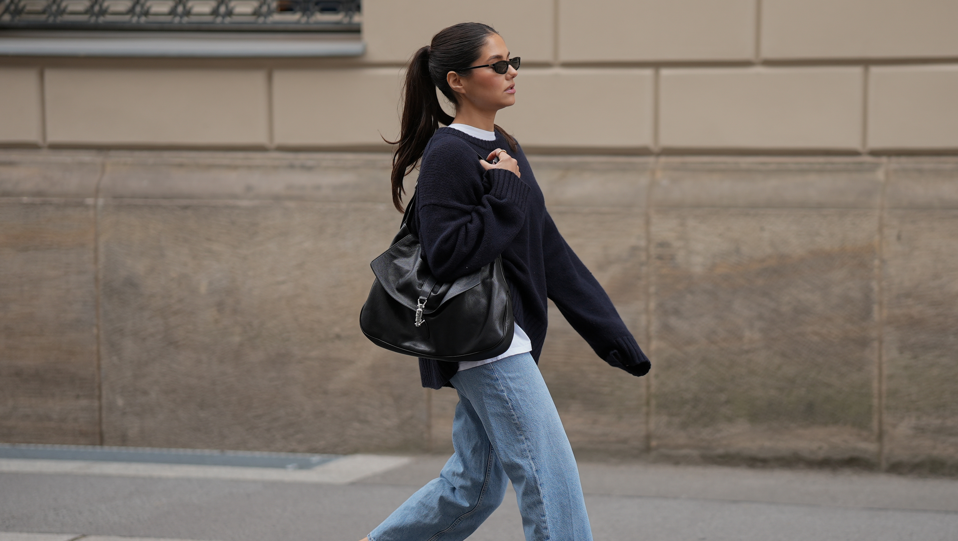 BERLIN, GERMANY - JULY 23: Aylin Sengül is seen wearing an oversized navy knit sweater from COS layered over a white crew neck T-shirt from Arket; light blue straight leg jeans from COS; black leather slingback loafers with CC logo hardware from Chanel; a black Jackie 1961 shoulder bag crafted from soft grained leather with a signature silver tone piston clasp from Gucci; black narrow rectangular sunglasses from Miu Miu on July 23, 2026 in Berlin, Germany. (Photo by Moritz Scholz/Getty Images)