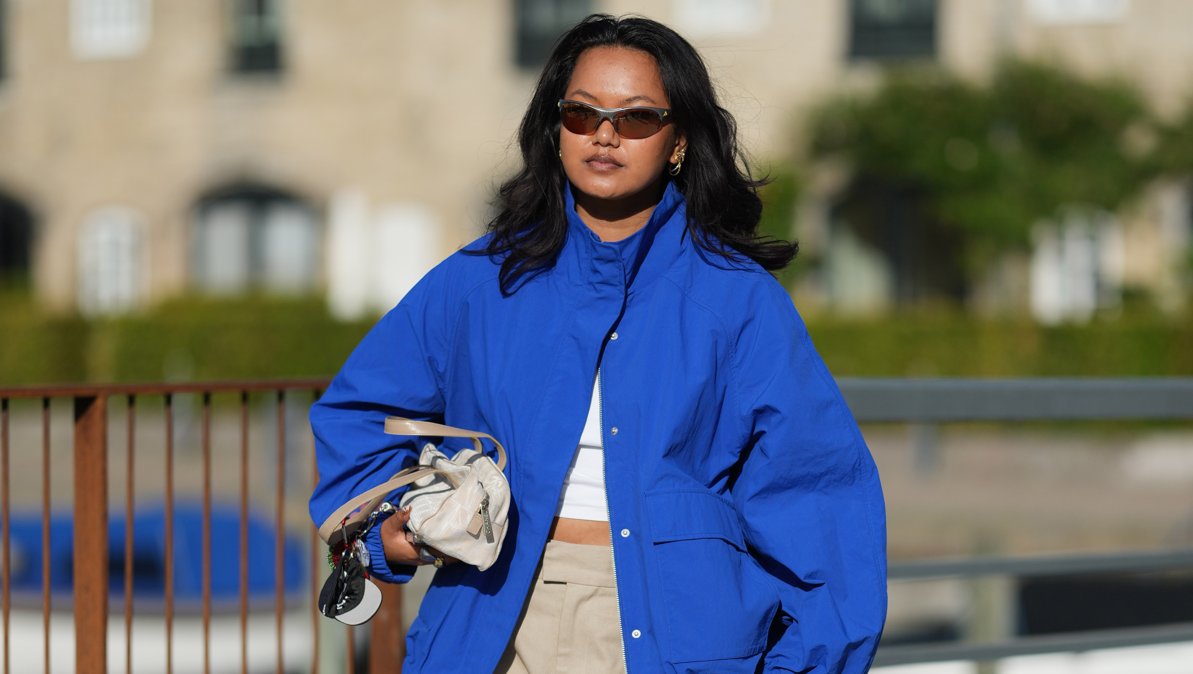 COPENHAGEN, DENMARK - JULY 06: A guest wears long wavy black hair with a center part, brown rectangular sunglasses with tinted lenses, a cobalt blue zip-front jacket with a high collar, a white crop top, beige wide-leg knee-length shorts, a Chanel beige crossbody bag, white leather lace-up ballet flat shoes, outside Collina Strada, during Copenhagen Fashion Week Spring/Summer 2027, on July 06, 2026 in Copenhagen, Denmark (Photo by Edward Berthelot/Getty Images)