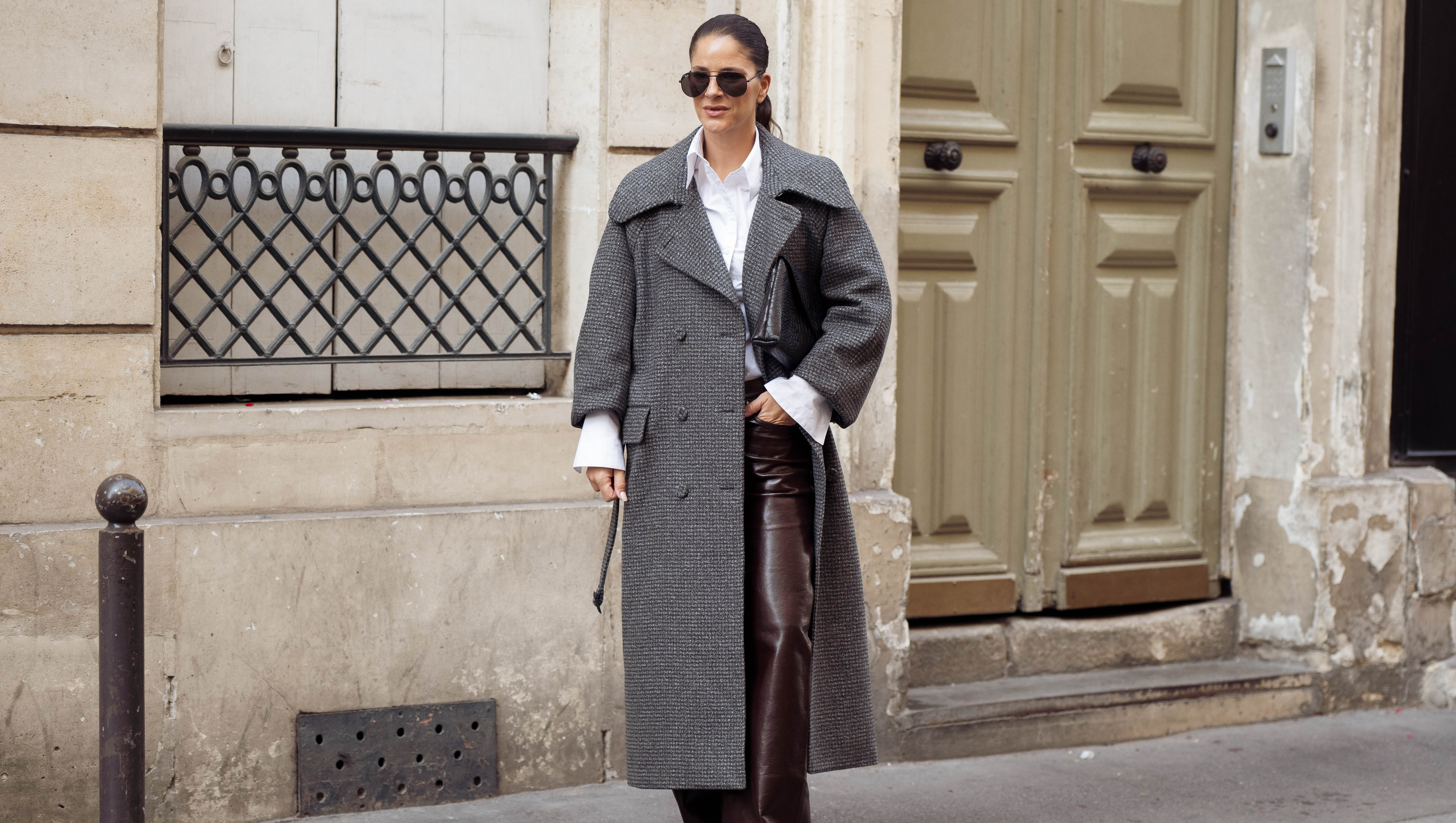 PARIS, FRANCE - OCTOBER 04: Gili Biegun wears a long grey textured coat over a white shirt, dark brown leather trousers, aviator sunglasses, and black pointed toe shoes during Day Seven of Paris Fashion Week - Womenswear Spring/Summer 2027 on October 04, 2026 in Paris, France. (Photo by Raimonda Kulikauskiene/Getty Images)